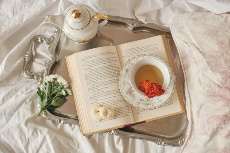 A silver tray with an open book and teacup sitting on a bed