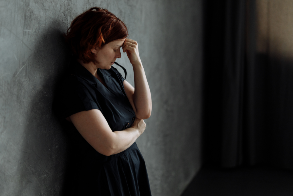 a woman in a black dress leaning against a wall holding her head