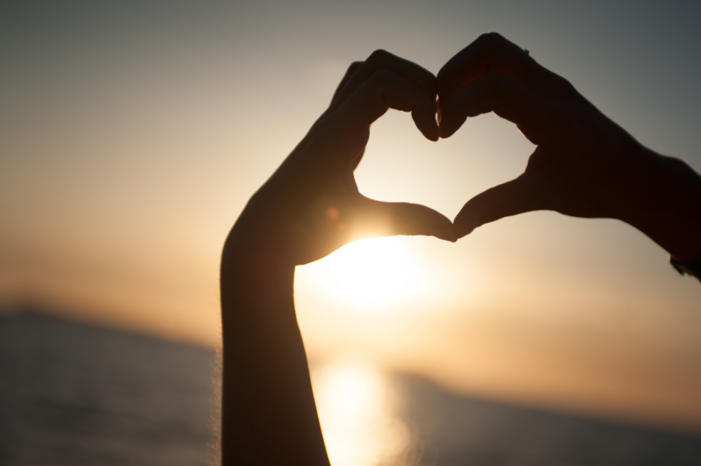 Two hands making a heart shape in front of a sunset