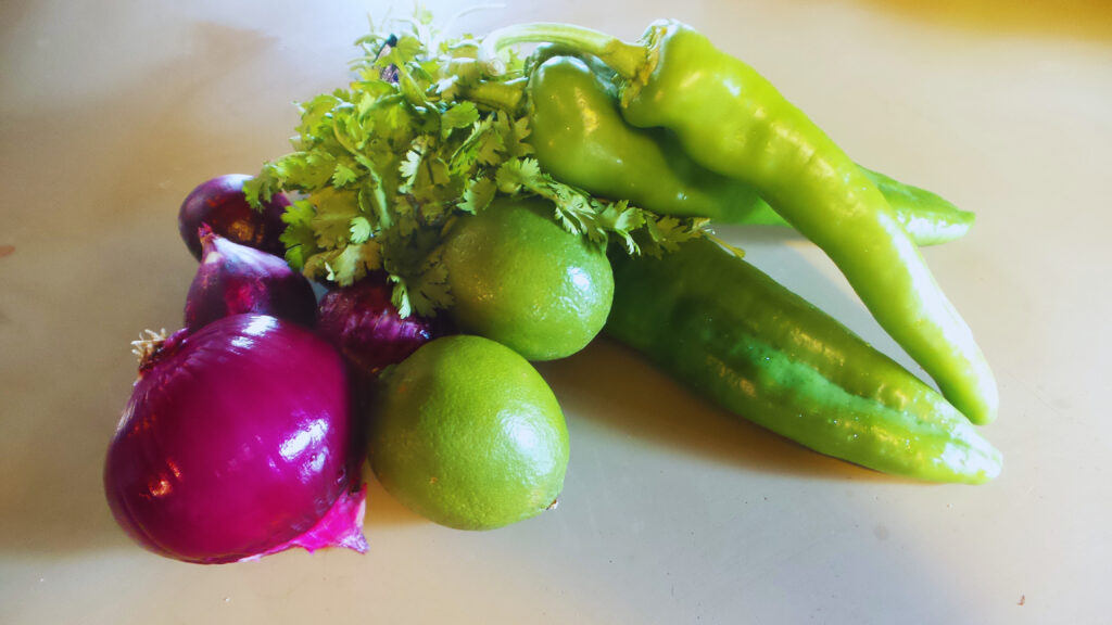 red onions, anaheim peppers, cilantro and lime sitting on a green countertop