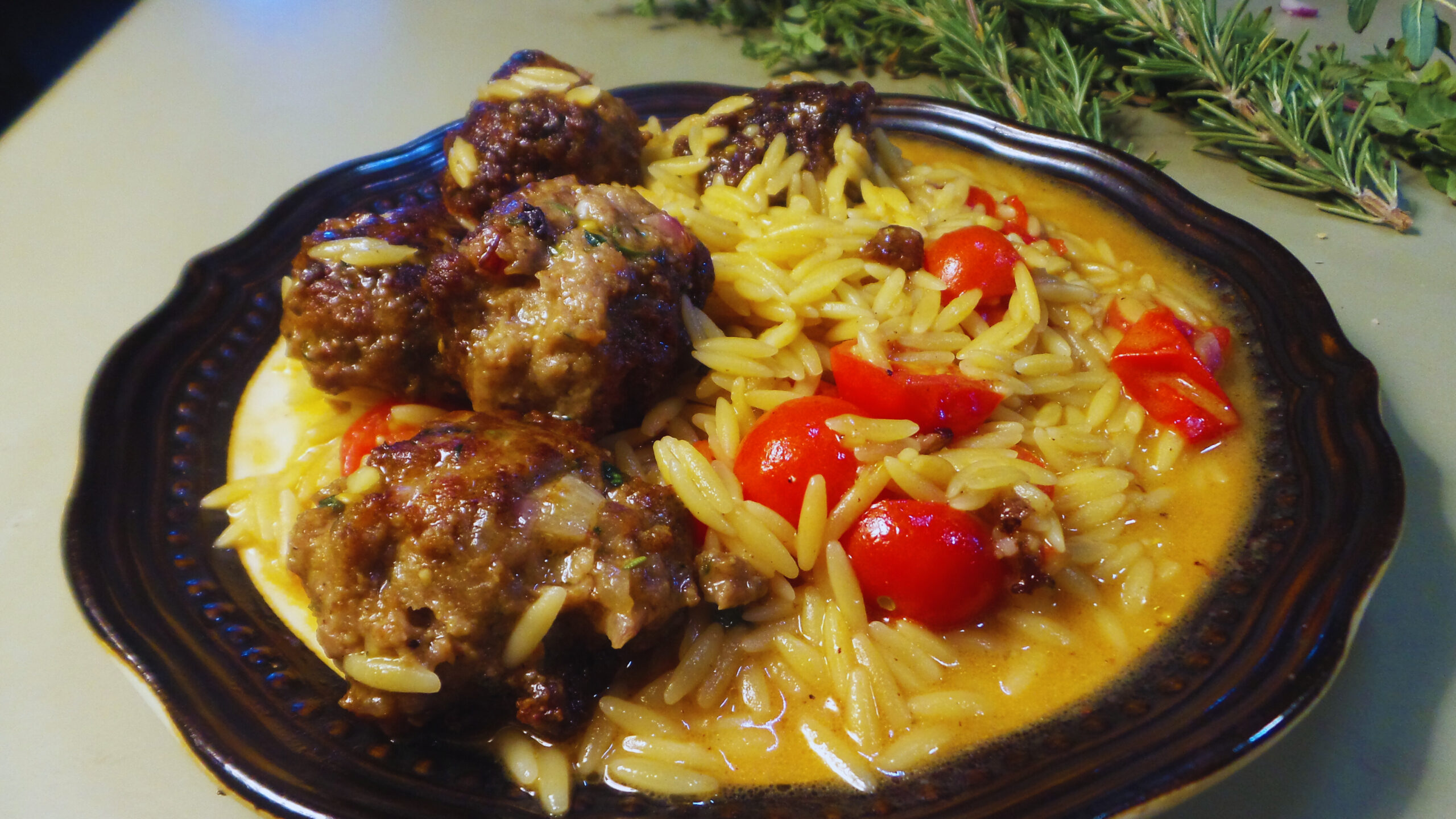 a plate of cooked meatballs, orzo and cherry tomatoes