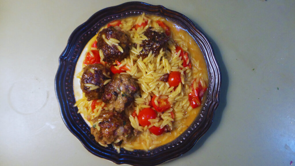 a plate of cooked meatballs, orzo and cherry tomatoes