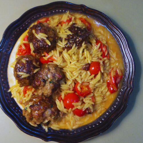 a plate of cooked meatballs, orzo and cherry tomatoes