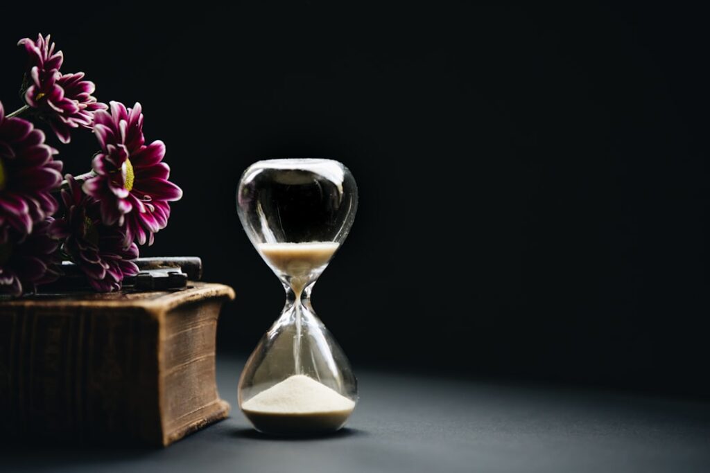 hourglass sitting next to purple flowers